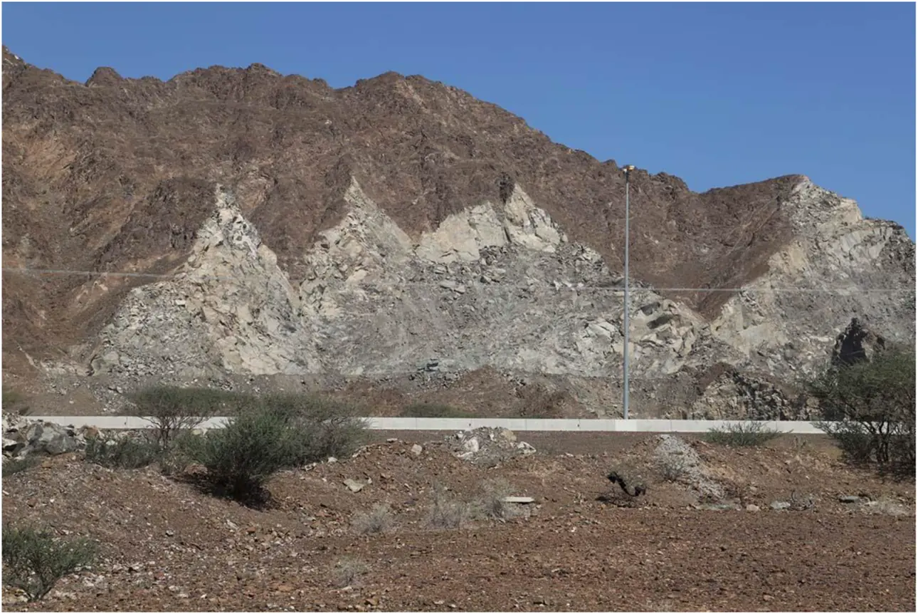 Pale exposed rock beneath a dark weathered ridge beside a road in an arid landscape