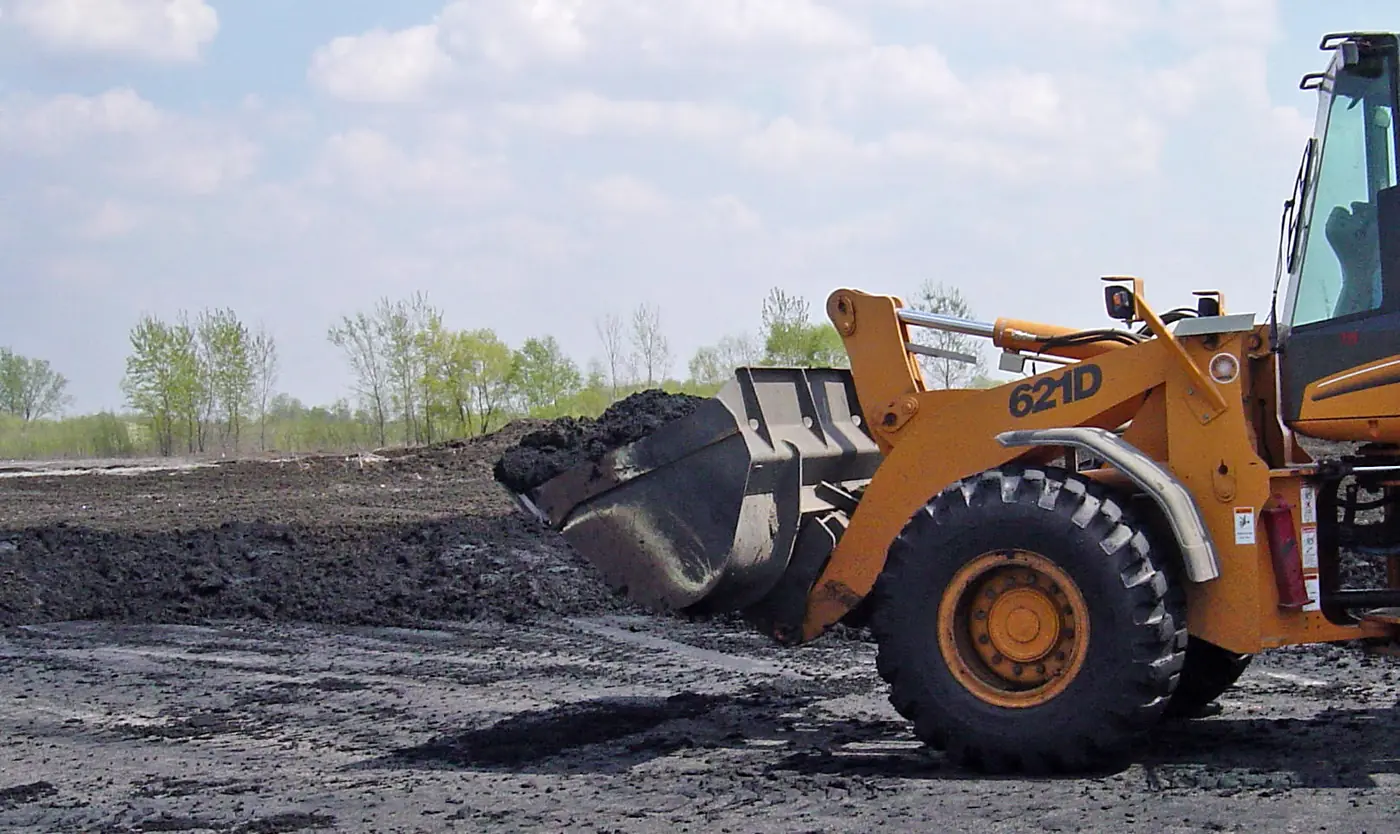 A front-end loader moves a pile of biosolids at a wastewater treatment site.