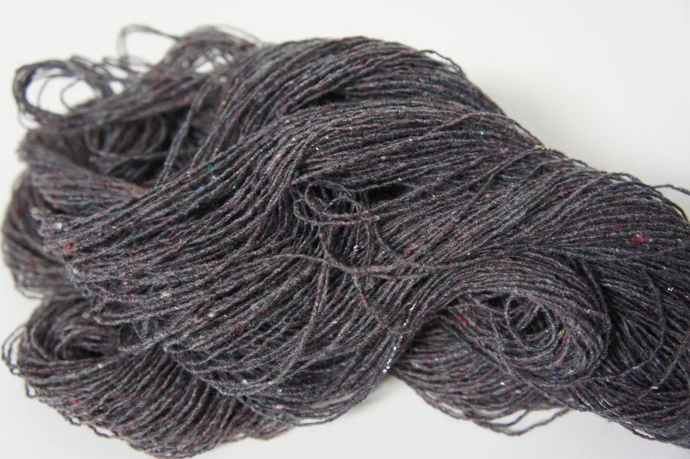 Dark grey recycled yarn with small flecks of colour wound into loose skeins