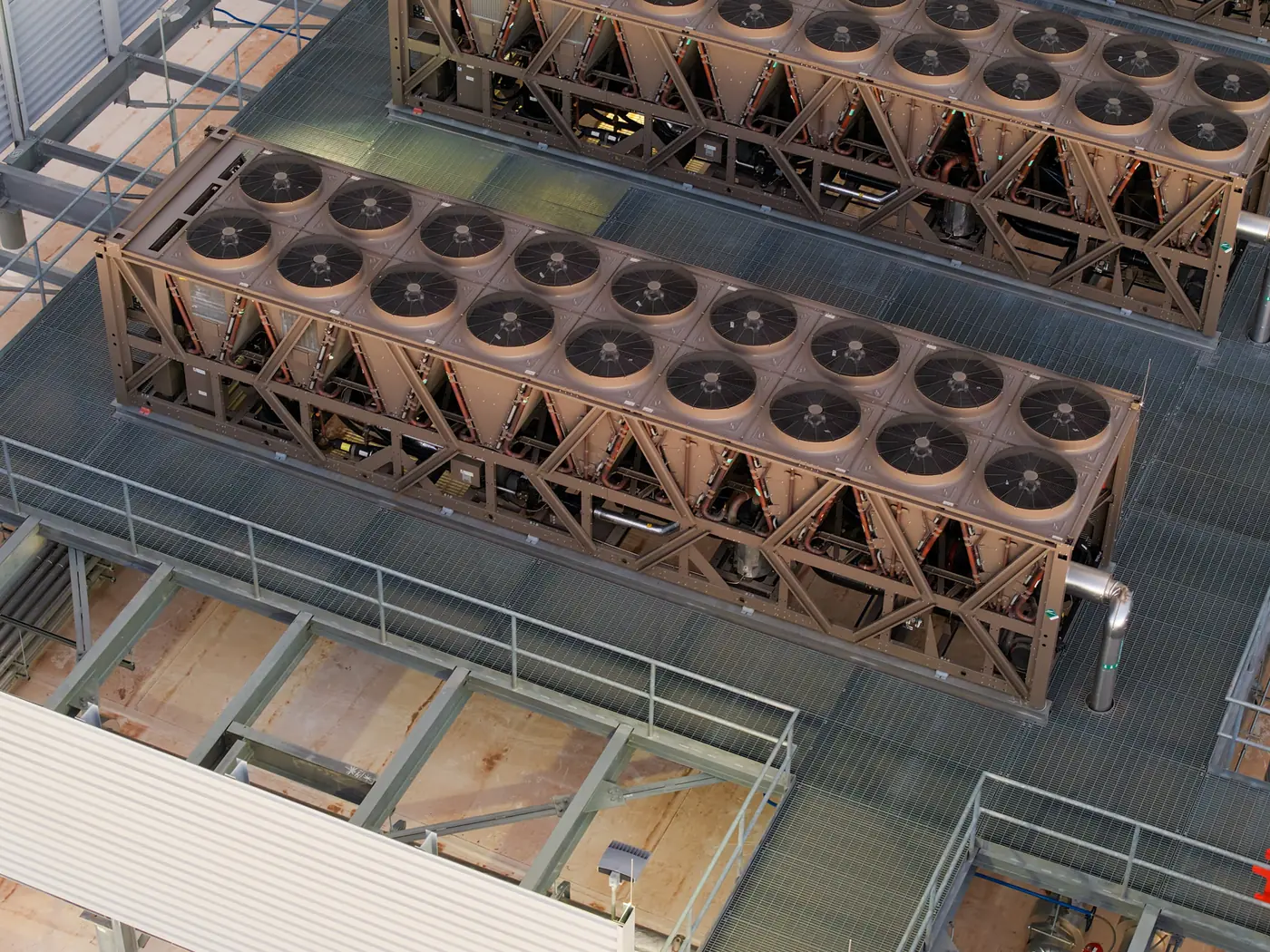 Rows of rooftop cooling units with large circular fans and connecting pipes.