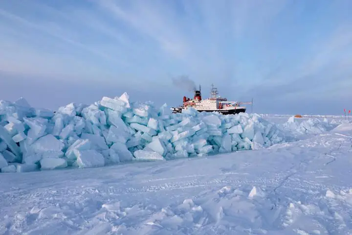 Blocks of blue-white sea ice piled into a pressure ridge, with the research icebreaker Polarstern behind them.