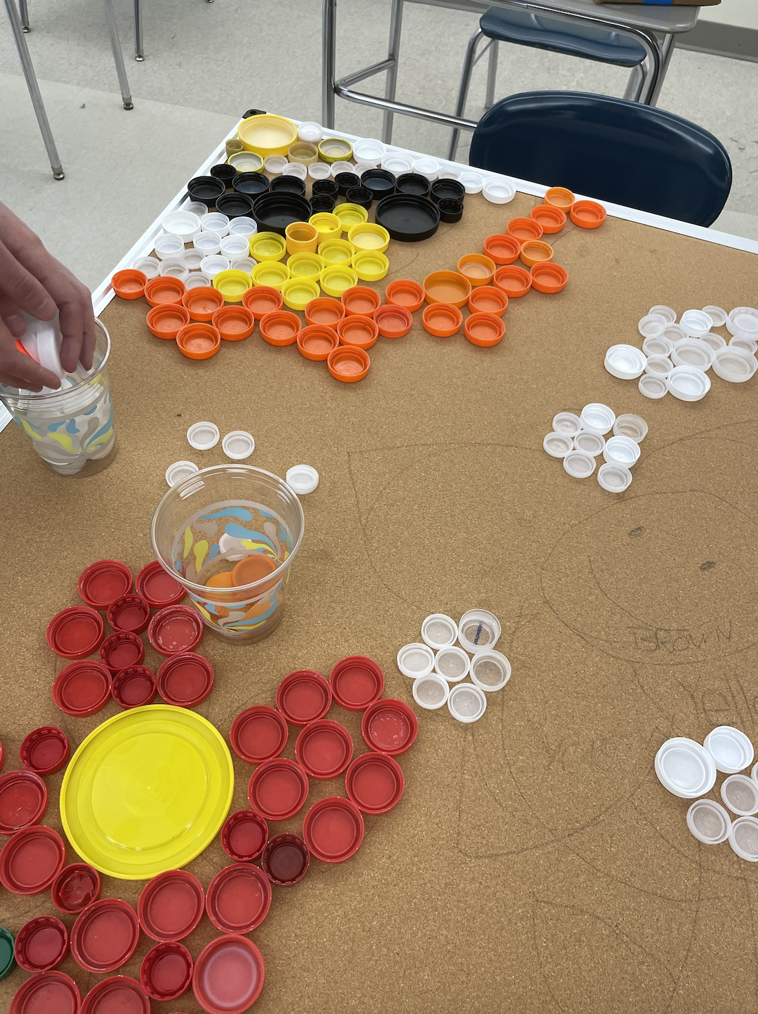 Students arranging orange, yellow, red, and white caps into shapes on a board